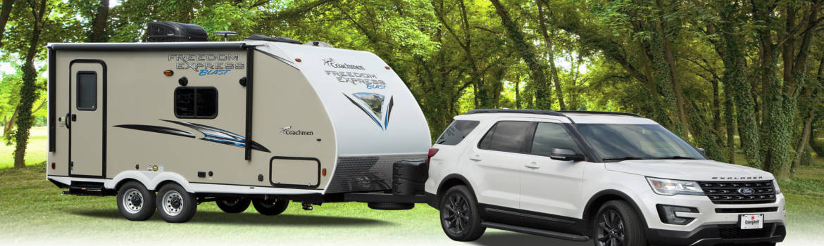 White Ford Explorer towing a 2018 coachmen Freedom-Express in forested area